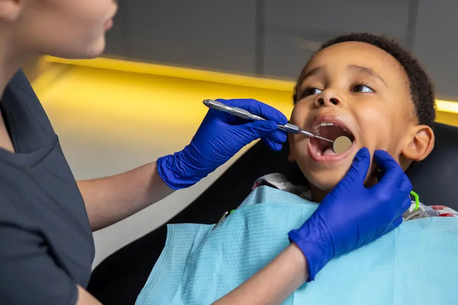 Criança em consulta odontológica, com o dentista examinando os dentes com espelho clínico.